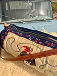 Embroidered bag with cowboy design in front of a vintage vehicle