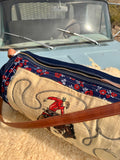 Embroidered bag with cowboy design in front of a vintage vehicle