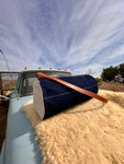 Vintage truck with a large blue duffel bag on a fluffy white rug under a blue sky.
