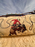 Embroidered fabric with a cowboy riding a horse design against a cloudy sky.
